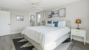 A bedroom with a bed, bedside tables, a ceiling fan, and framed pictures on the wall. - Entire 6BR Beach Duplex | Walk to Beach | Sleeps 12 (Bradenton Beach)