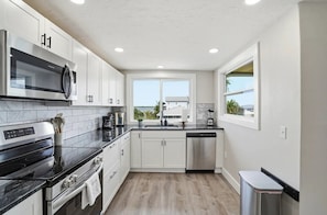 A modern kitchen with white cabinets, a stainless steel refrigerator, a microwave, a stove, and a dishwasher.