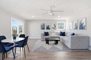 A modern living room with a sectional sofa, a dining table with chairs, and a ceiling fan. - Entire 6BR Beach Duplex | Walk to Beach | Sleeps 12 (Bradenton Beach)