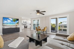 A modern living room with a flat-screen TV, a dining area with chairs, a sofa, and a balcony with a view.