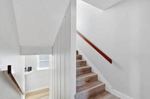 A staircase with wooden steps and a wooden handrail, leading to a room with white walls and a window.