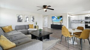 A modern living room with a grey sectional sofa, a black coffee table, and a dining area with yellow chairs. - Entire 6BR Beach Duplex | Walk to Beach | Sleeps 12 (Bradenton Beach)