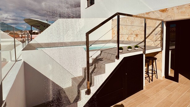 Ein moderner Außenpoolbereich mit geometrischem Design, einer Glasbrüstung und einer Steinmauer.