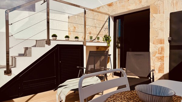 Un área de estar moderna al aire libre con una escalera que conduce a una entrada cubierta, plantas en macetas y vistas al cielo.