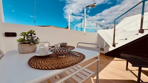 Eine Dachterrasse mit Tisch für zwei Personen, mit Topfpflanze, Schale und Tasse.