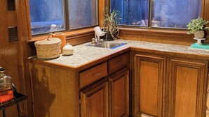 A kitchen with wooden cabinets, a countertop, and a window with a view of a backyard.