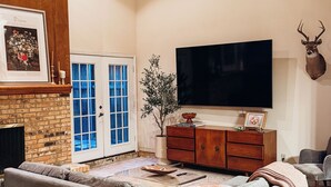 A living room with a sectional sofa, a flat-screen TV, a mounted deer head, a fireplace, and a blue-framed door.