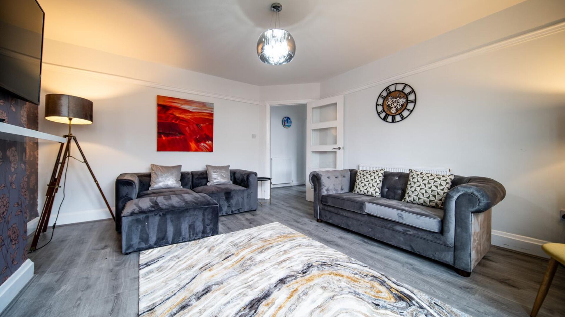 A modern living room with two grey sofas, a marble-patterned rug, a red abstract painting, and a wall clock.