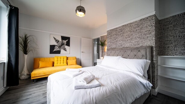 A modern bedroom with a bed, a yellow sofa, and a patterned wall.