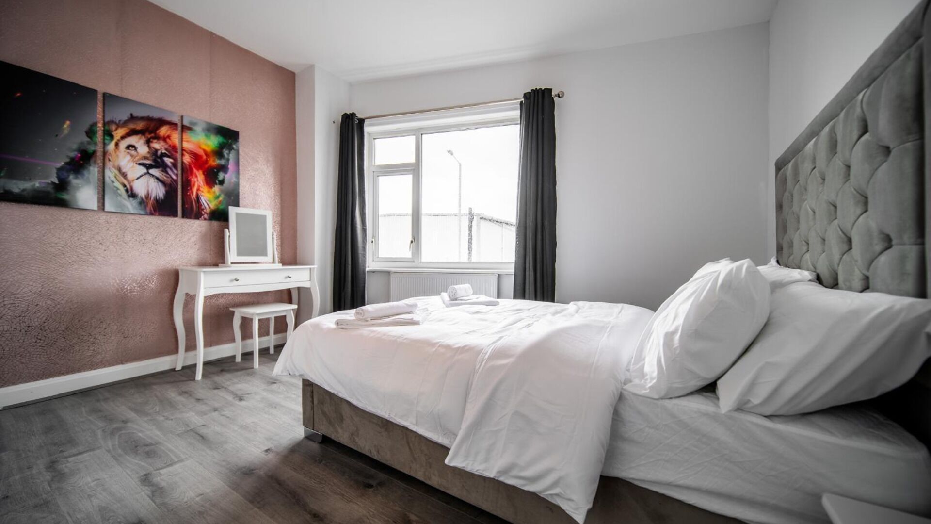 A modern hotel room with a large bed, a desk, and a window with curtains.