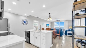 A modern kitchen with white cabinetry, a central island, and a dining area with blue furniture.