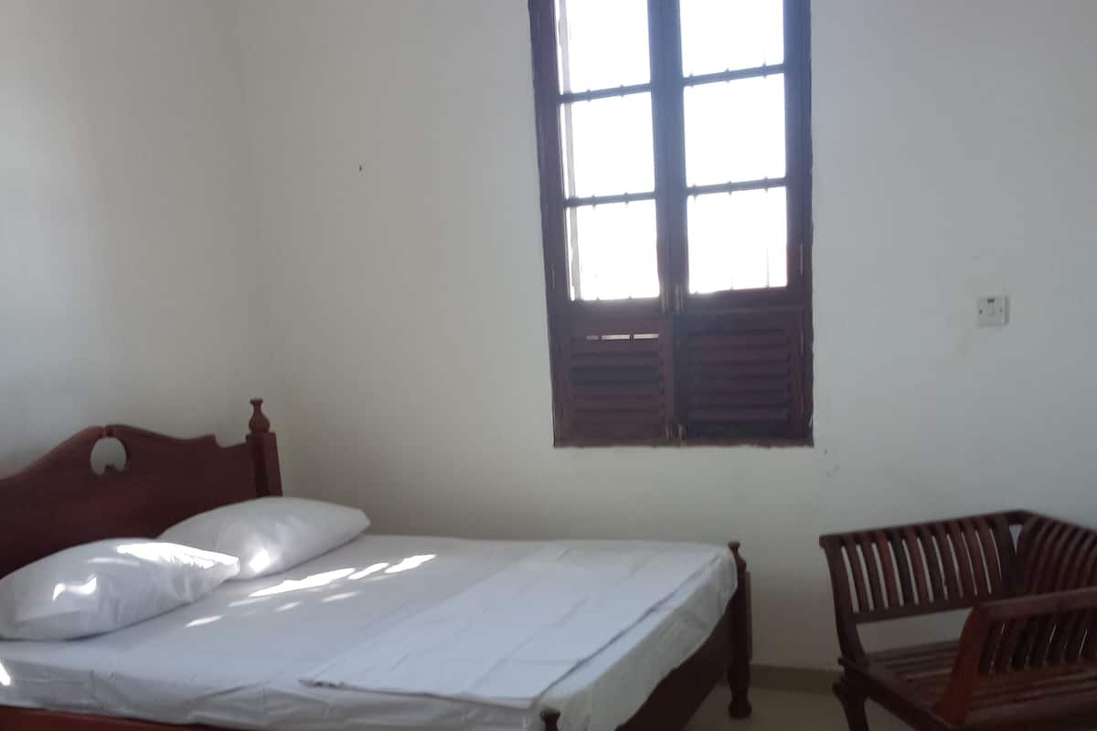 Una habitación con una cama y una silla de madera, y una ventana con contraventanas de madera.