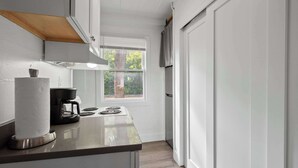 A narrow kitchen with white cabinets, a built-in stove, and a window with a view of trees.