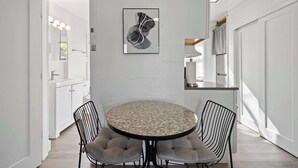 A modern kitchen with white cabinetry, a round dining table with cushioned chairs, and a framed abstract artwork on the wall.