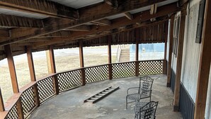 A covered outdoor area with a concrete floor, wooden beams, metal chairs, and a wooden fence.