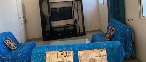 A living room with a sofa set, a coffee table covered with printed papers, a ceiling fan, and a television.