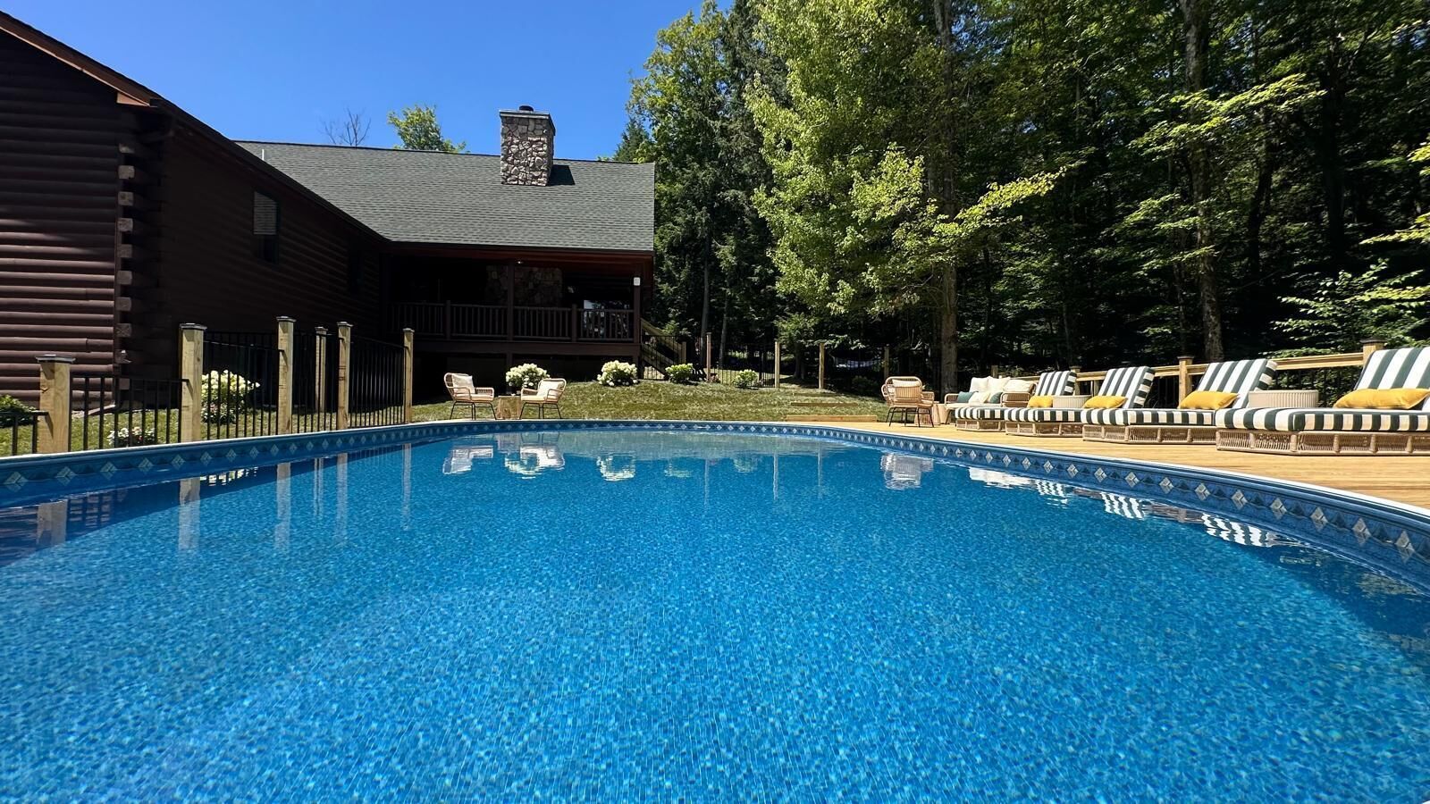 Une piscine d’un bleu éclatant, avec des chaises longues et un bâtiment en bois en arrière-plan.