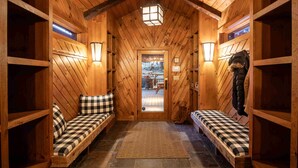 Ein Interieur einer Holzhütte mit einer karierten Bank, einer Tür, die nach draußen führt, und einem Laternenlicht an der Decke.