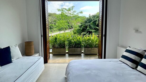 A bedroom with a bed, a sofa, and a view of a garden through an open door. - Yeguas 102 by Wynwood House (Anapoima)