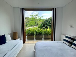 A bedroom with a bed, a sofa, and a view of a garden through an open door. - Yeguas 102 by Wynwood House (Anapoima)