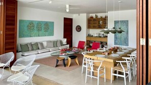 A modern living room with a sofa, dining table, and chairs. There is a painting on the wall and a bookshelf in the background. - Yeguas 102 by Wynwood House (Anapoima)