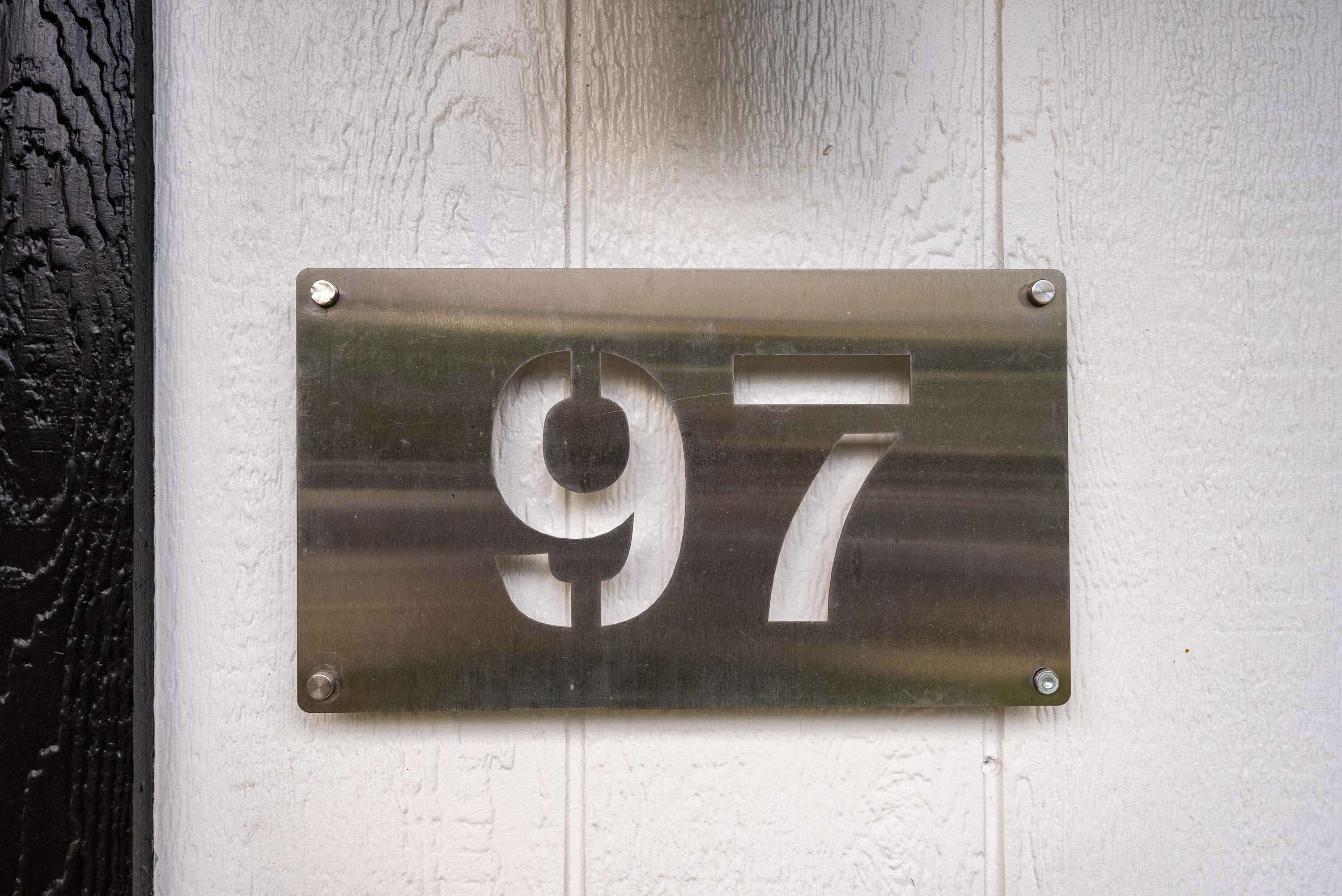 Placa de porta com o número 97, em metal, fixada numa parede branca.