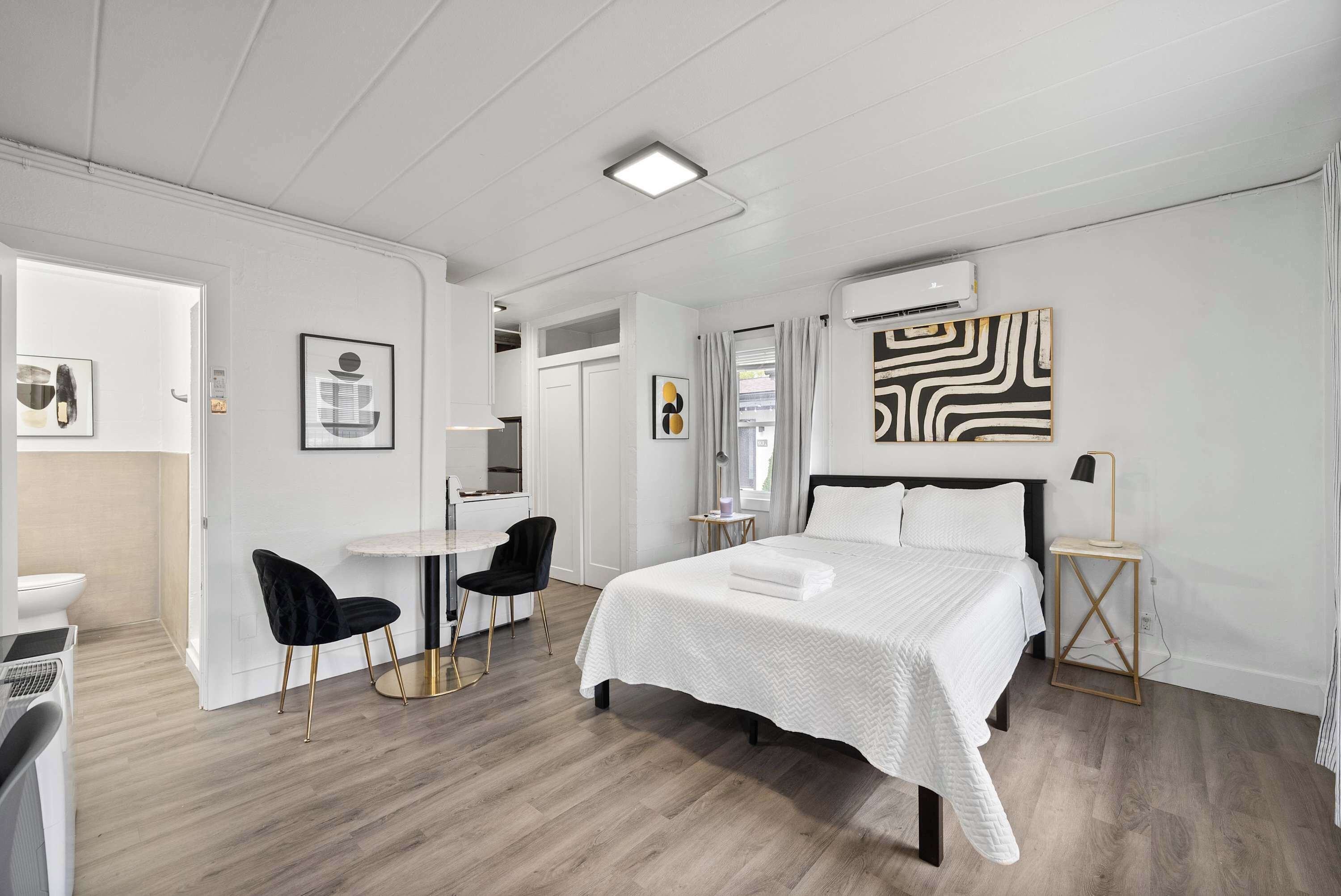 A modern hotel room with a large bed, a desk, a chair, and artwork on the walls.