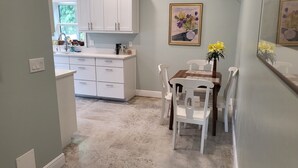 A kitchen with white cabinets, a dining table with chairs, and a vase with yellow flowers on the wall.