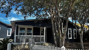 A two-story house with a porch, a white picket fence, and a tree in front.