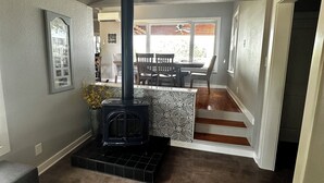 A living room with a black wood-burning stove, a dining area with a table and chairs, and a kitchen area with a patterned backsplash.