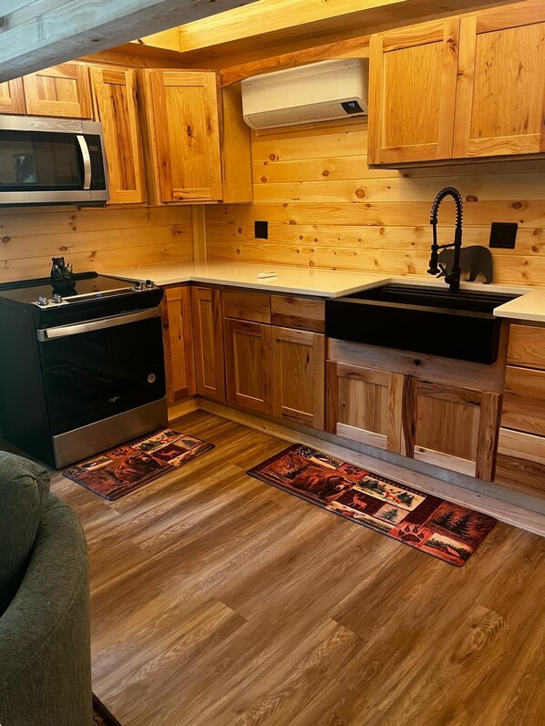Cocina compacta con armarios de madera, microondas, estufa y lavamanos.