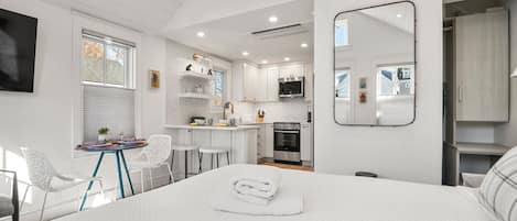 A modern hotel room with a large bed, a small kitchenette, and a dining area.