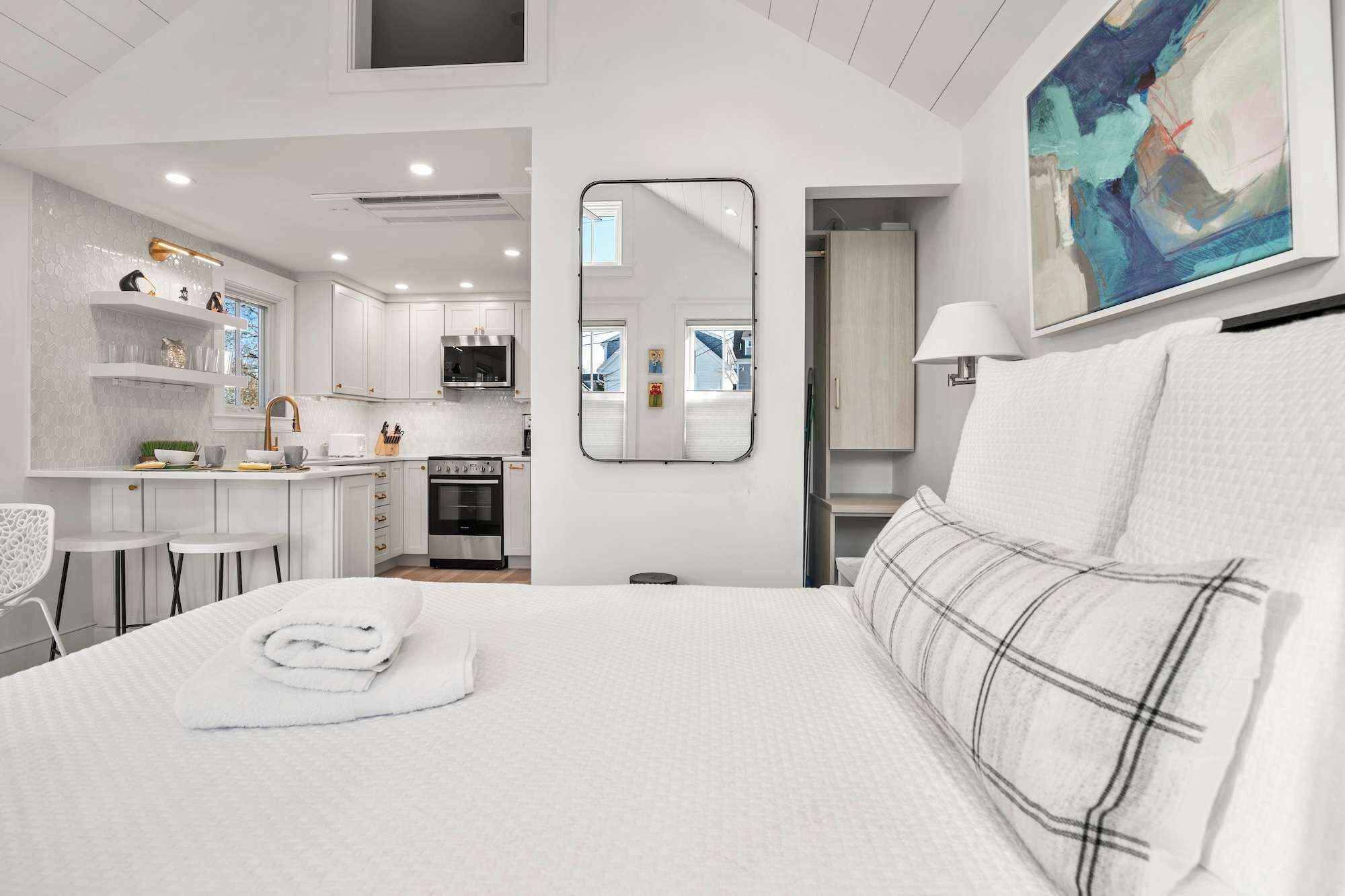 A modern hotel room with a large bed, a small kitchenette, and a bathroom visible through an open door.