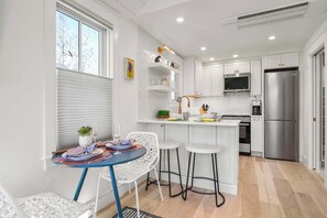 Une cuisine moderne avec des meubles blancs, un réfrigérateur en acier inoxydable et un coin bar équipé de tabourets.
