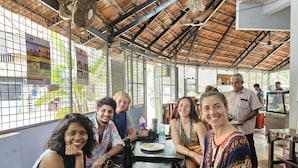 A group of people seated at a table inside a building with a thatched roof and metal mesh walls. - The Hostel Stories Varkala (Varkala)