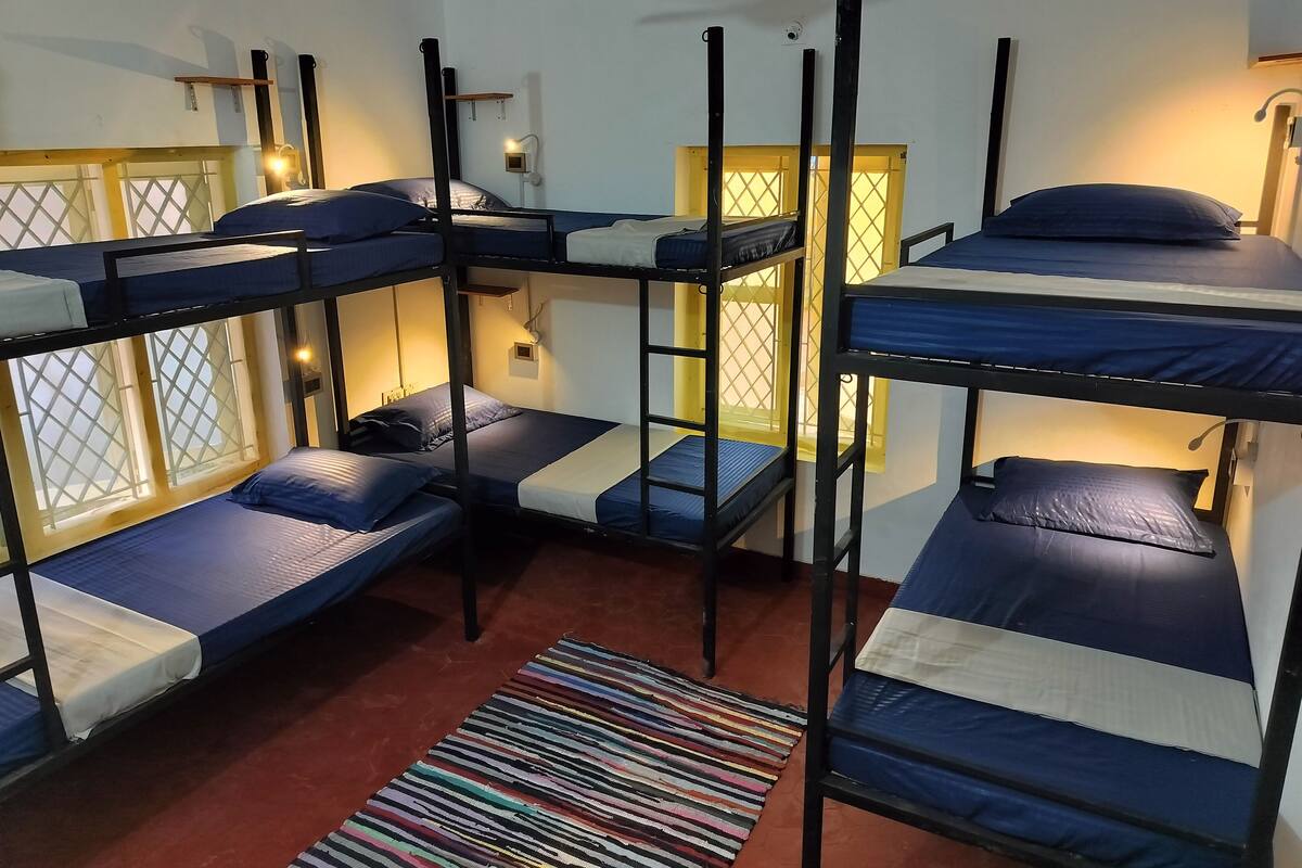A dormitory room with bunk beds, a ceiling fan, and a window with a lattice design.