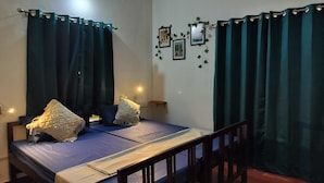 A single bed with a wooden headboard, dark curtains, and a bedside table with a lamp. - The Hostel Stories Varkala (Varkala)