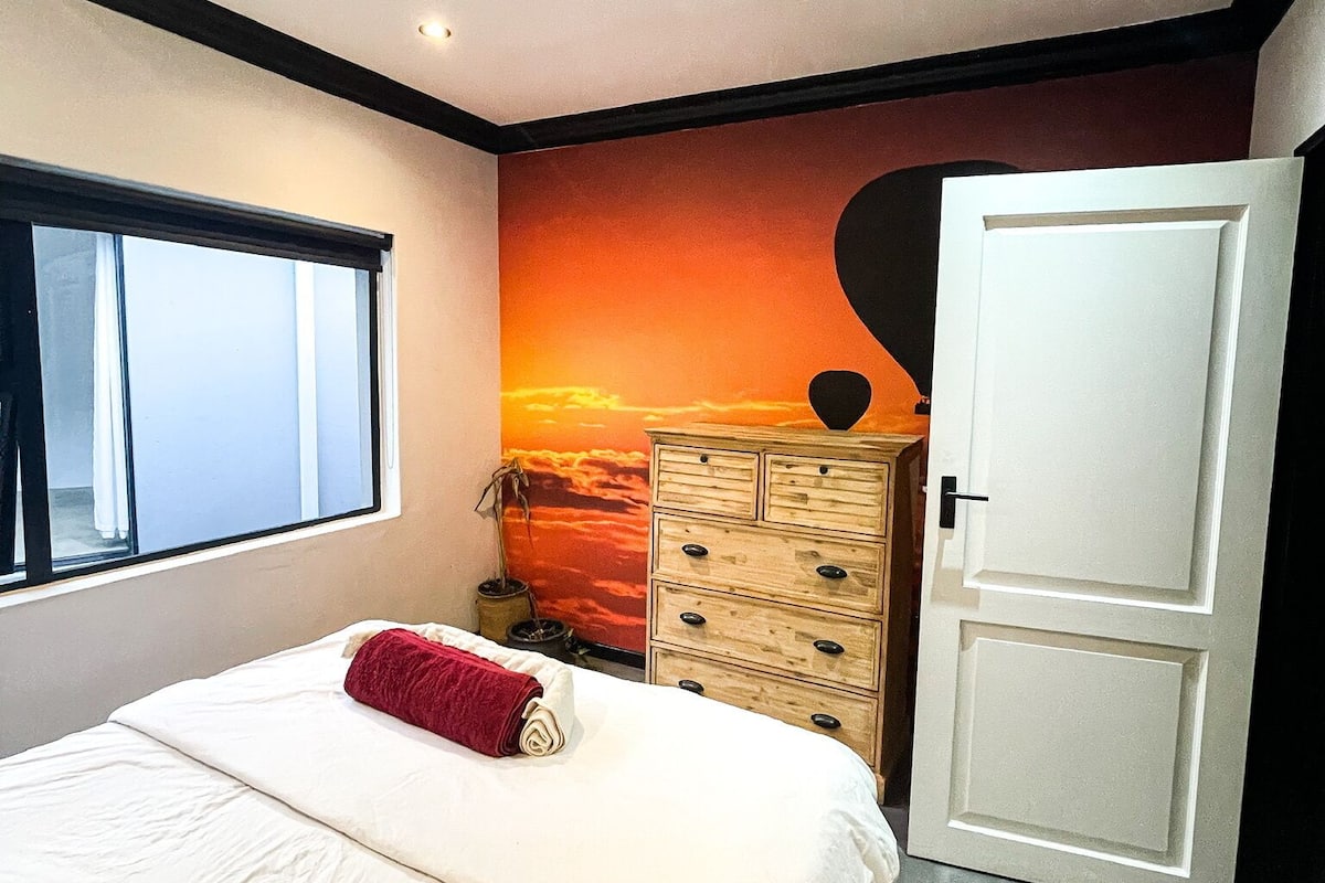 A bedroom with a bed, a dresser, a window, and a door.