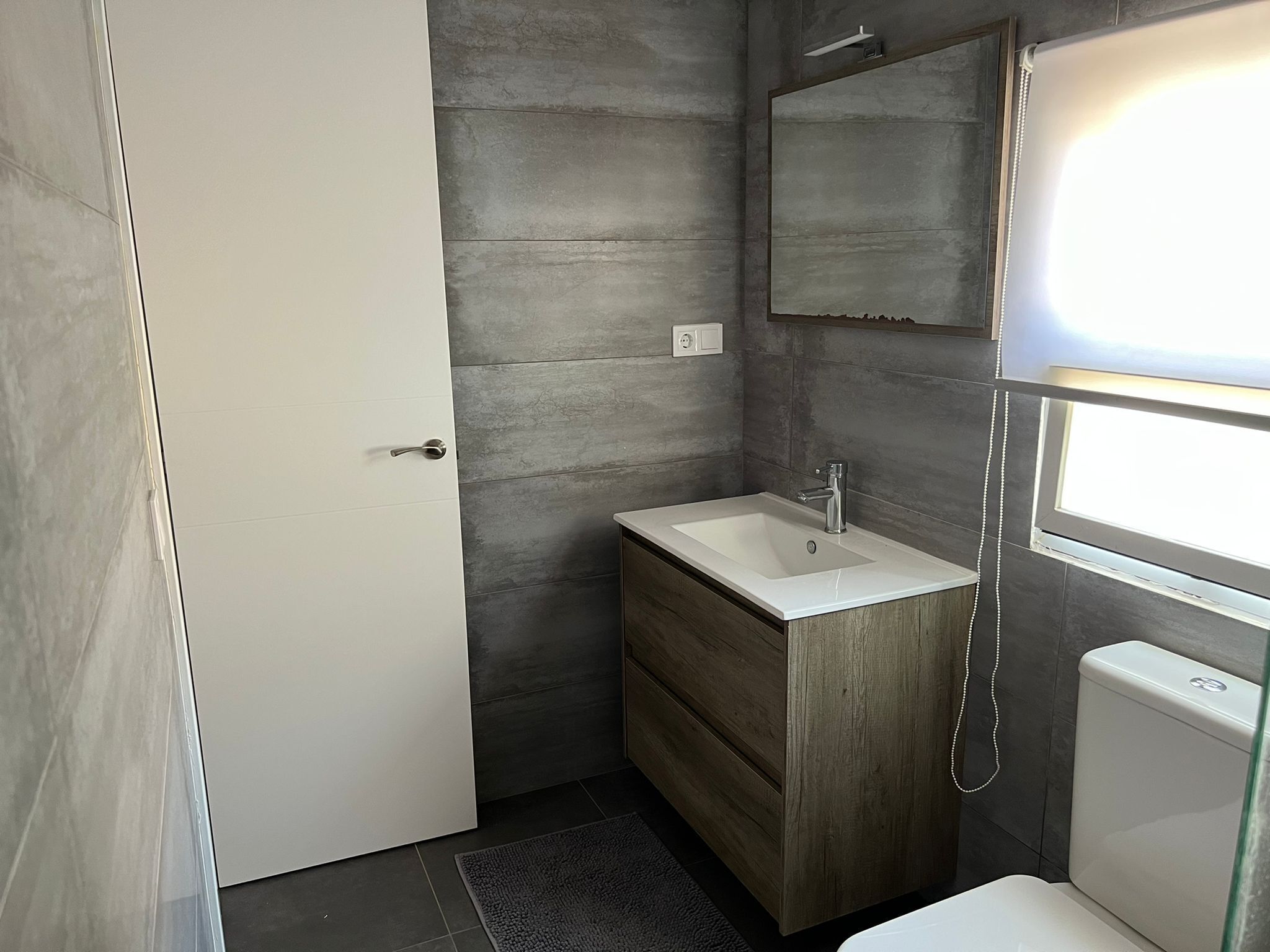 Ein modernes Badezimmer mit einem weißen Waschbecken, einem Holz-Waschtisch und einem Spiegel darüber.