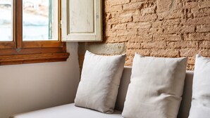 A white sofa with three cushions against a brick wall and a window with wooden frames.