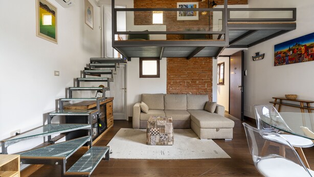 Ein Loft-Wohnraum mit Schlafgalerie, einer Couch, einem Glastisch und einem Essbereich inklusive Tisch und Stühlen.