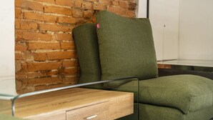Ein grünes Sofa vor einer Ziegelwand, ein Holztisch daneben und ein Glastrennzaun.