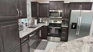 A modern kitchen with dark wood cabinets, stainless steel appliances, granite countertops, and a patterned rug. - Maximo Vacation

 (North Port)