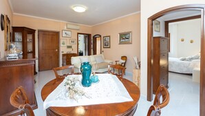 A dining area with a wooden table, chairs, and a blue vase. There is a sofa and a bed in the background. - Apartment in Via Genova in Ladispoli a few steps from the sea and train station (Ladispoli)