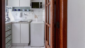 Μια μικρή κουζίνα με λευκά ντουλάπια, ένα φούρνο μικροκυμάτων, μια καφετιέρα και έναν νεροχύτη.