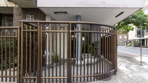 Μια πύλη με μεταλλική περίφραξη, ένα πλακόστρωτο μονοπάτι και ένας δρόμος με ένα κίτρινο αυτοκίνητο και μια διάβαση πεζών.