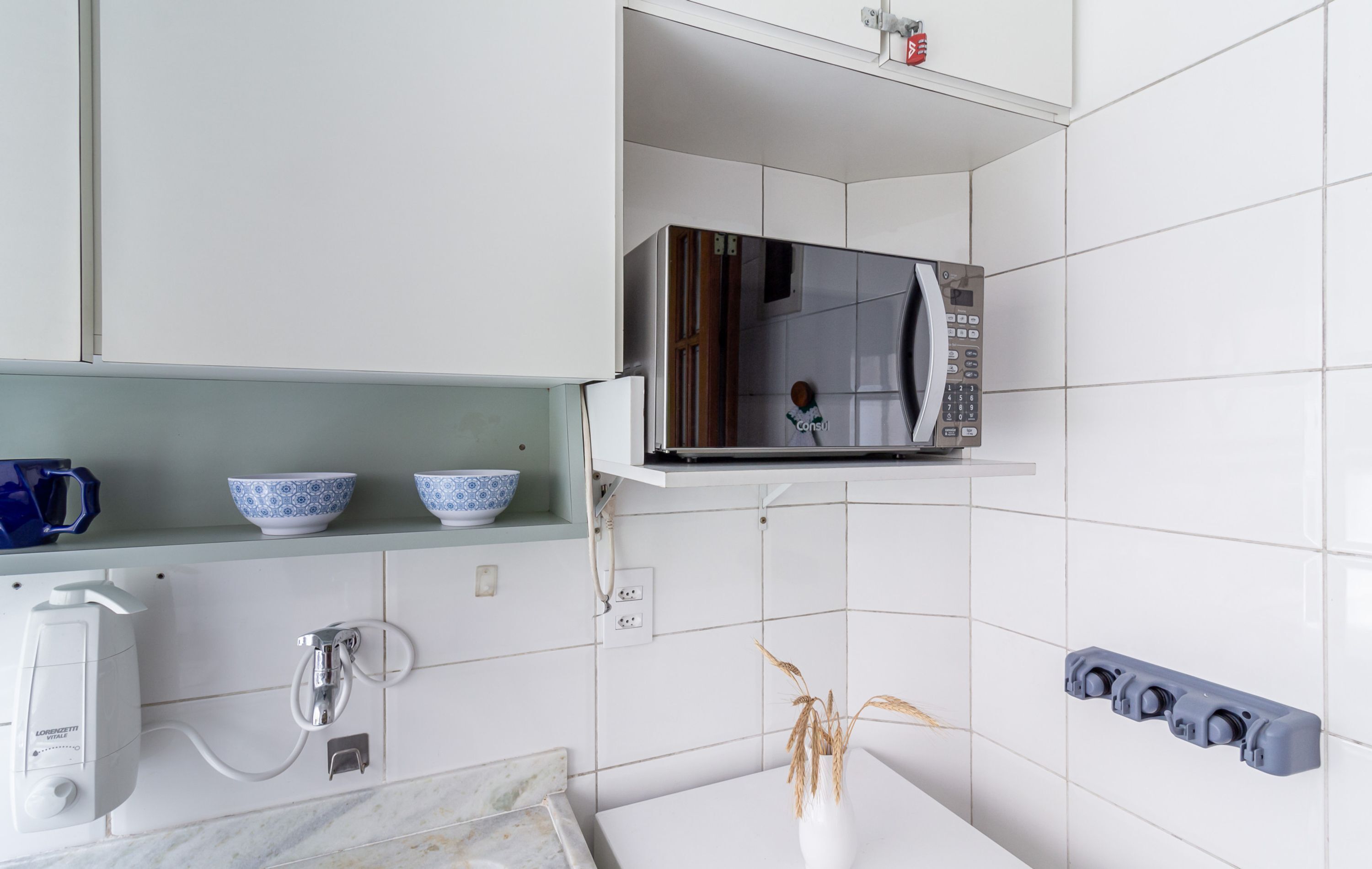 A kitchen with white tiles, a microwave, a coffee machine, and a shelf with blue and white bowls.