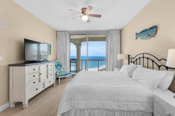A bedroom with a bed, a dresser, a chair, a television, and a view of the ocean.