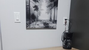 Un bureau en bois, avec une machine à café et un tableau représentant une forêt accroché au mur.