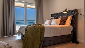 Een slaapkamer met een bed, een bedlampje en uitzicht op de zee door grote ramen.